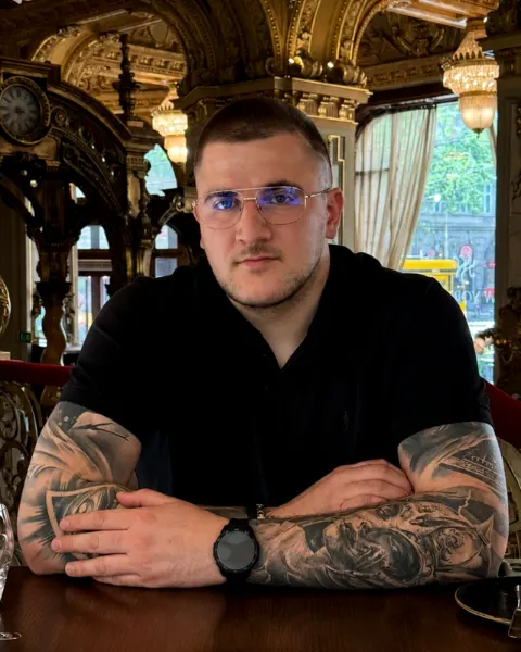 Wiktor Ślusarczyk przy stoliku w kawiarni, w okularach i czarnej koszulce.